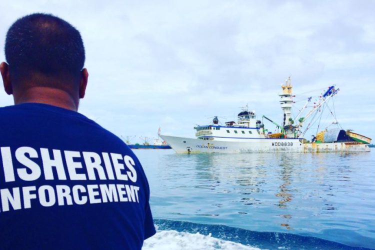 Tuna fisheries compliance officer with back turned to camera, in foreground, with tuna fishing vessel in water, Marshall Islands. Photo Francisco Blaha.