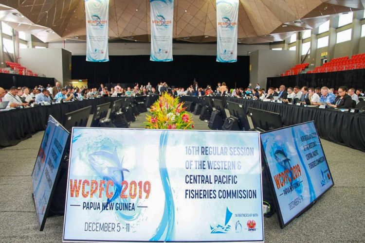 Inside the 16th Tuna Commission meeting in Port Moresby. Boards and banners displaying the words WCPFC 2019, and many people seated around the end of a room, with tables in a U formation. Photo: F. Tauafialfi.