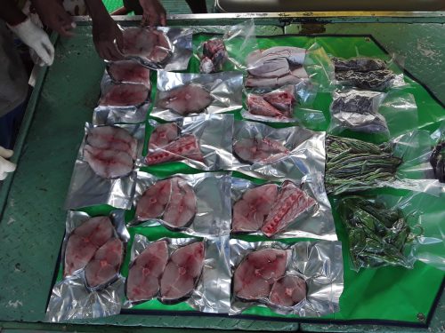 Vacuum packed pieces of tuna for sale at a market laid out on a table near vegetables