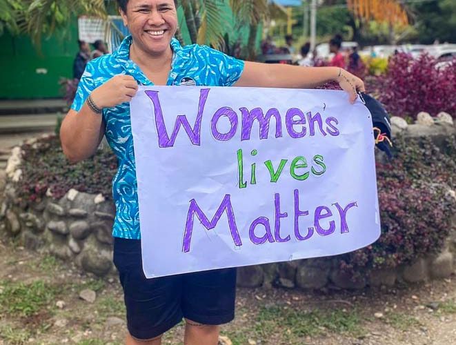 Joyce Samuela Ah-Leong, a fisheries management adviser with FFA, stands outside holding a home-made poster that says 'Women's lives matter'