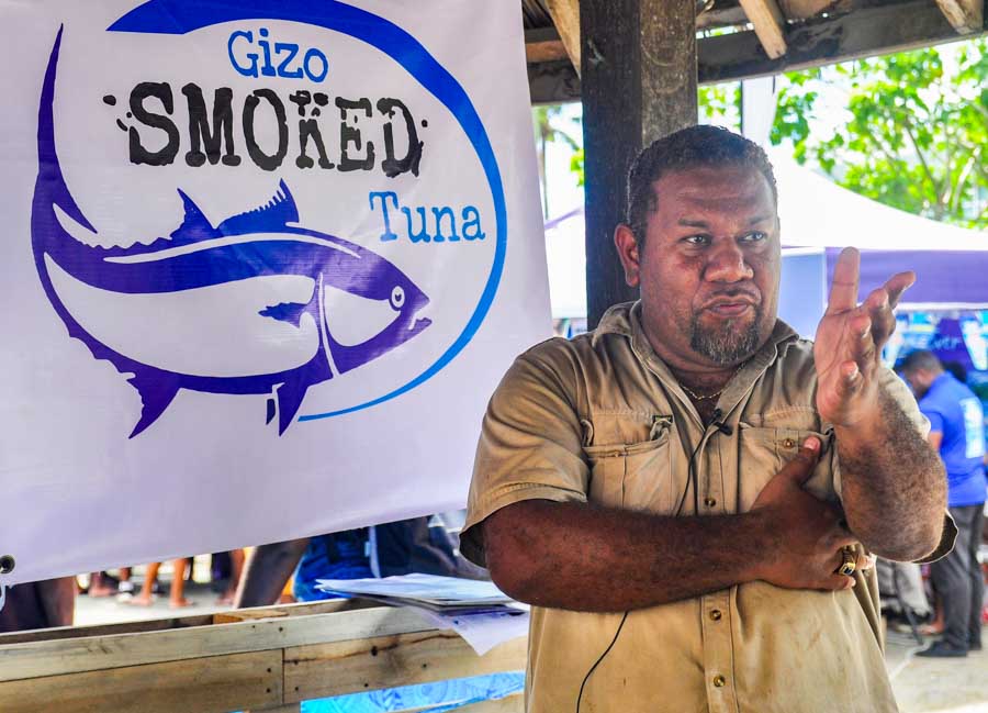 Solomon Islands man Schulte Maetoloa stands in front of sign that reads Gizo Smoked Tuna